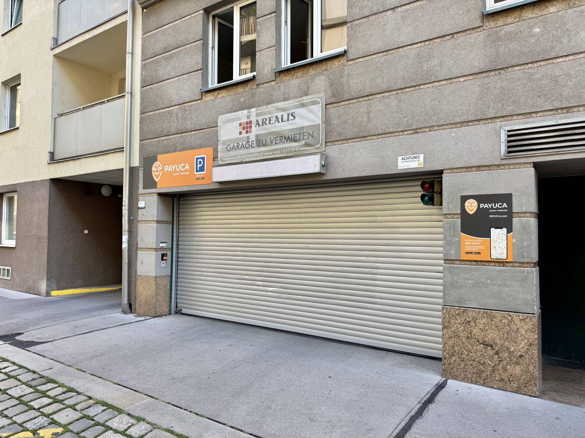 Garageneinfahrt mit Rolltor und Schildern für Mietangebote und Parksysteme.