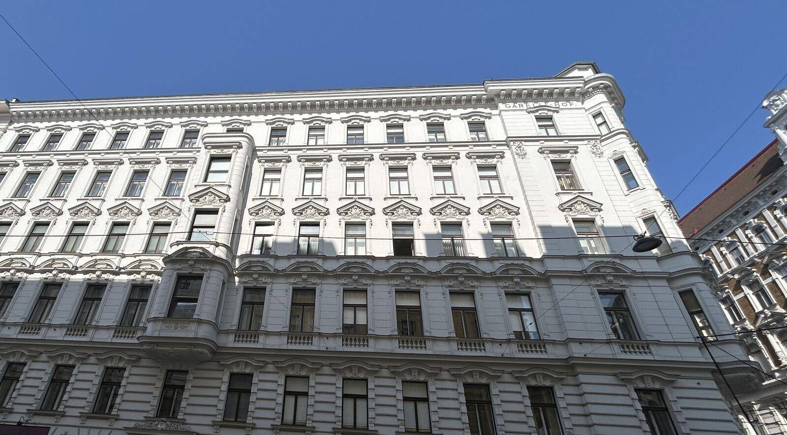 Historische Fassade eines Altbaus mit vielen Fenstern und dekorativen Elementen unter blauem Himmel.