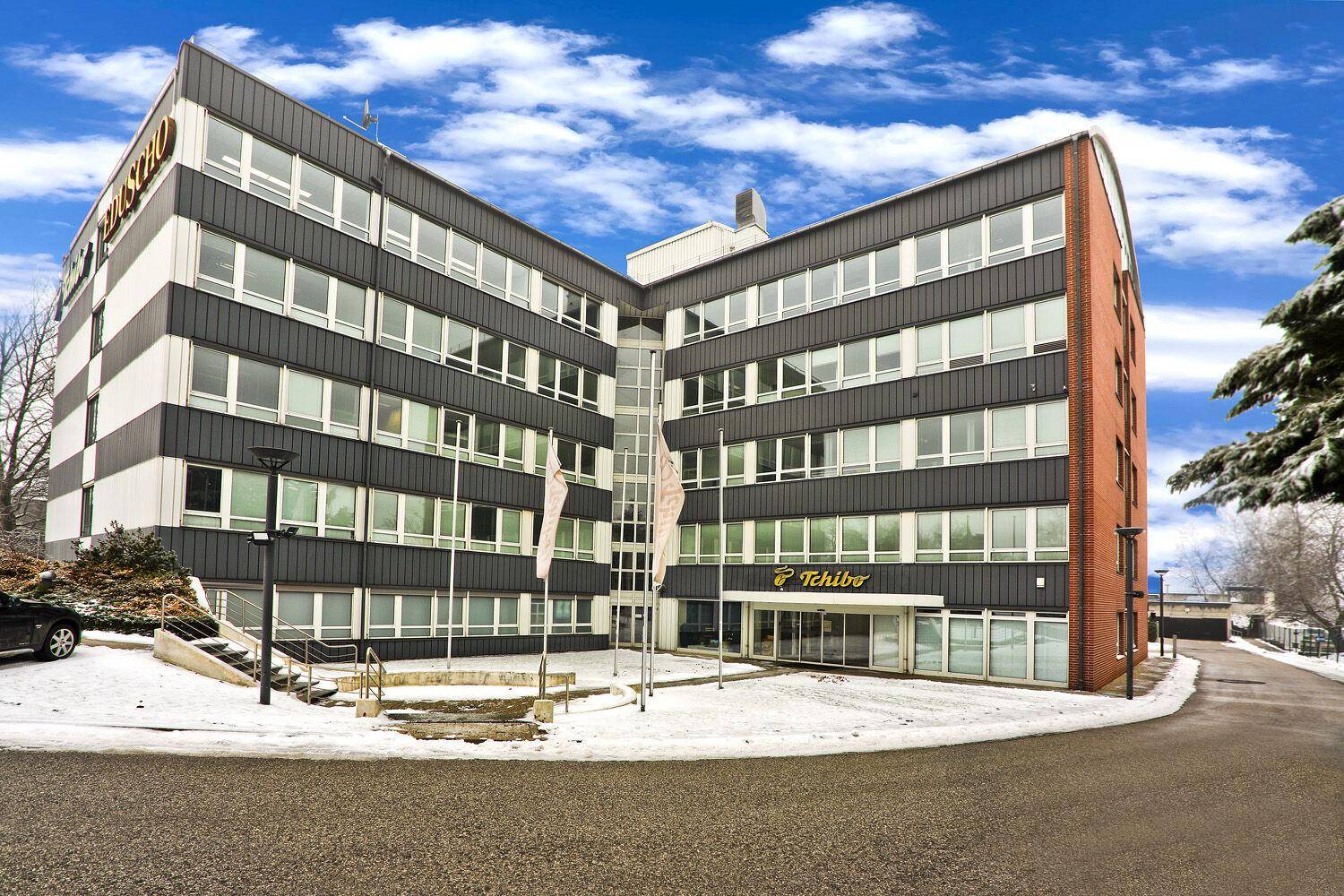 Großes Bürogebäude mit dunkler Fassade und vielen Fenstern, umgeben von Schnee und einer Zufahrt.