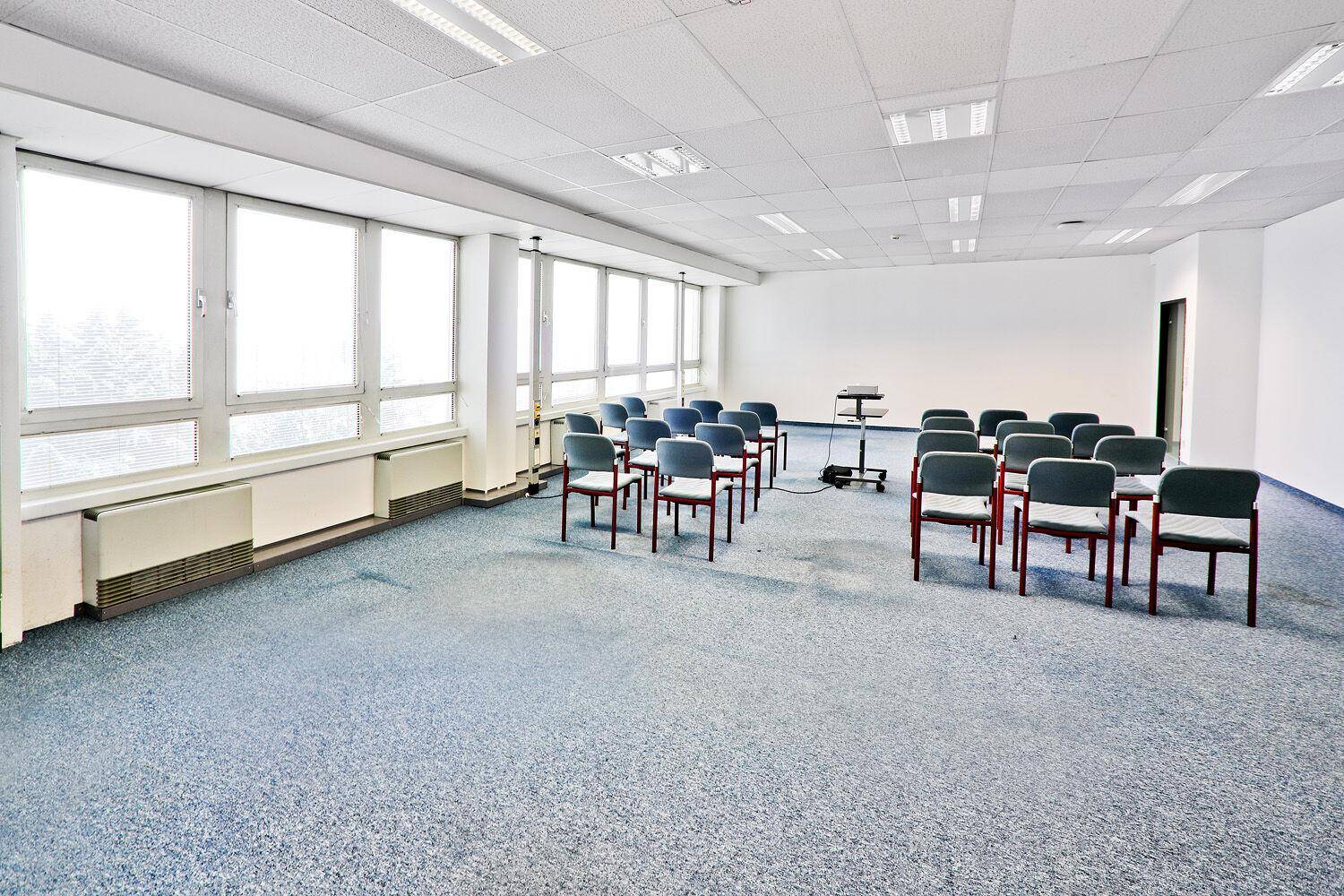 Konferenzraum mit blauem Teppichboden, Stuhlreihen, Projektor und großen Fenstern.