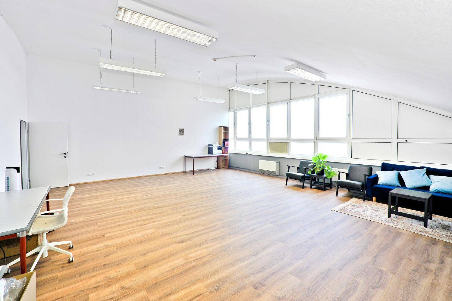 Geräumiger Aufenthaltsbereich mit Holzboden, blauen Sofas, Schreibtischen und großen Fenstern.