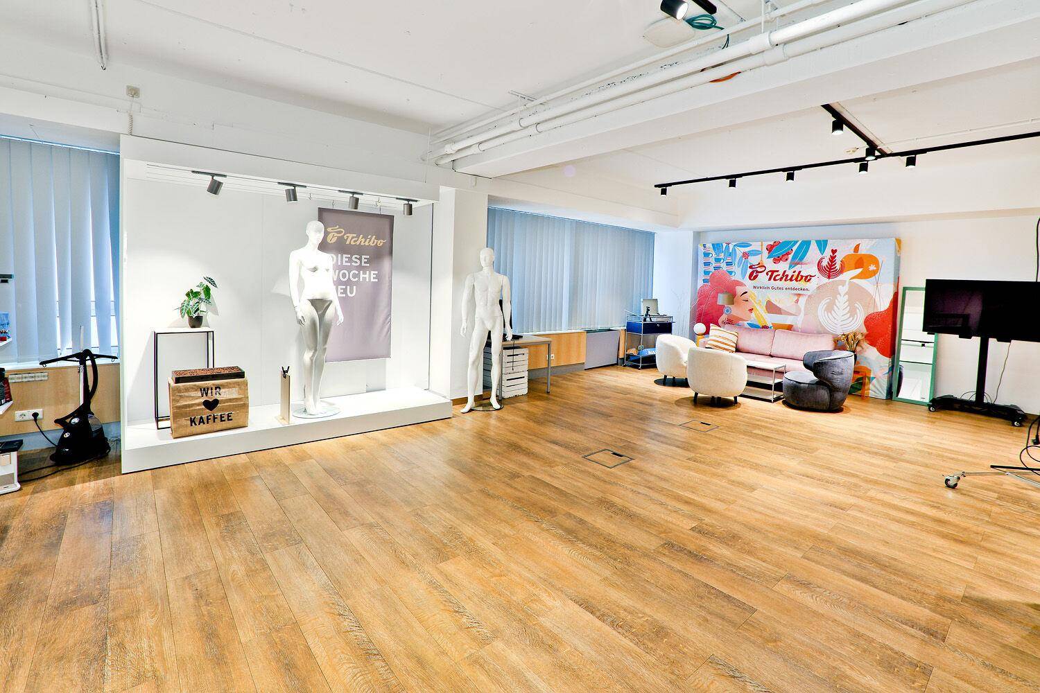 Großer Verkaufsraum mit Holzboden, Schaufensterpuppen, Sitzgelegenheiten und Werbebannern.