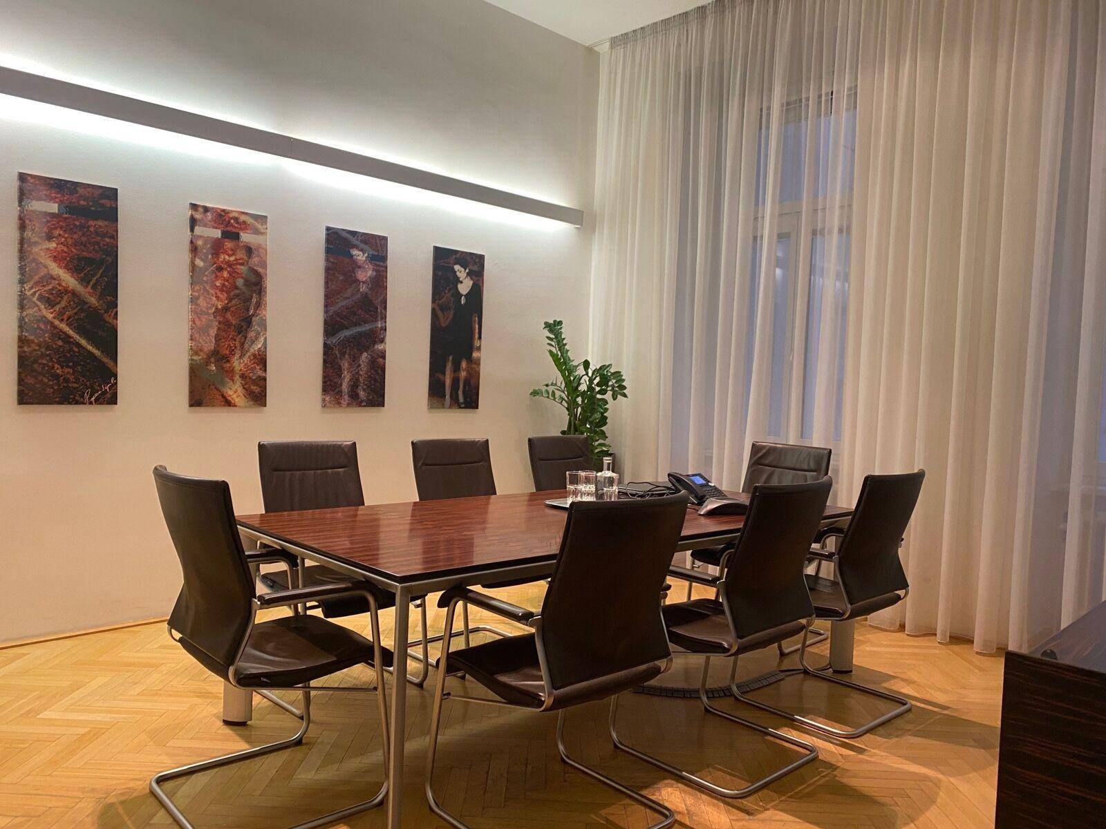 Besprechungszimmer mit großem Holztisch, bequemen Lederstühlen und eleganten Vorhängen am Fenster.