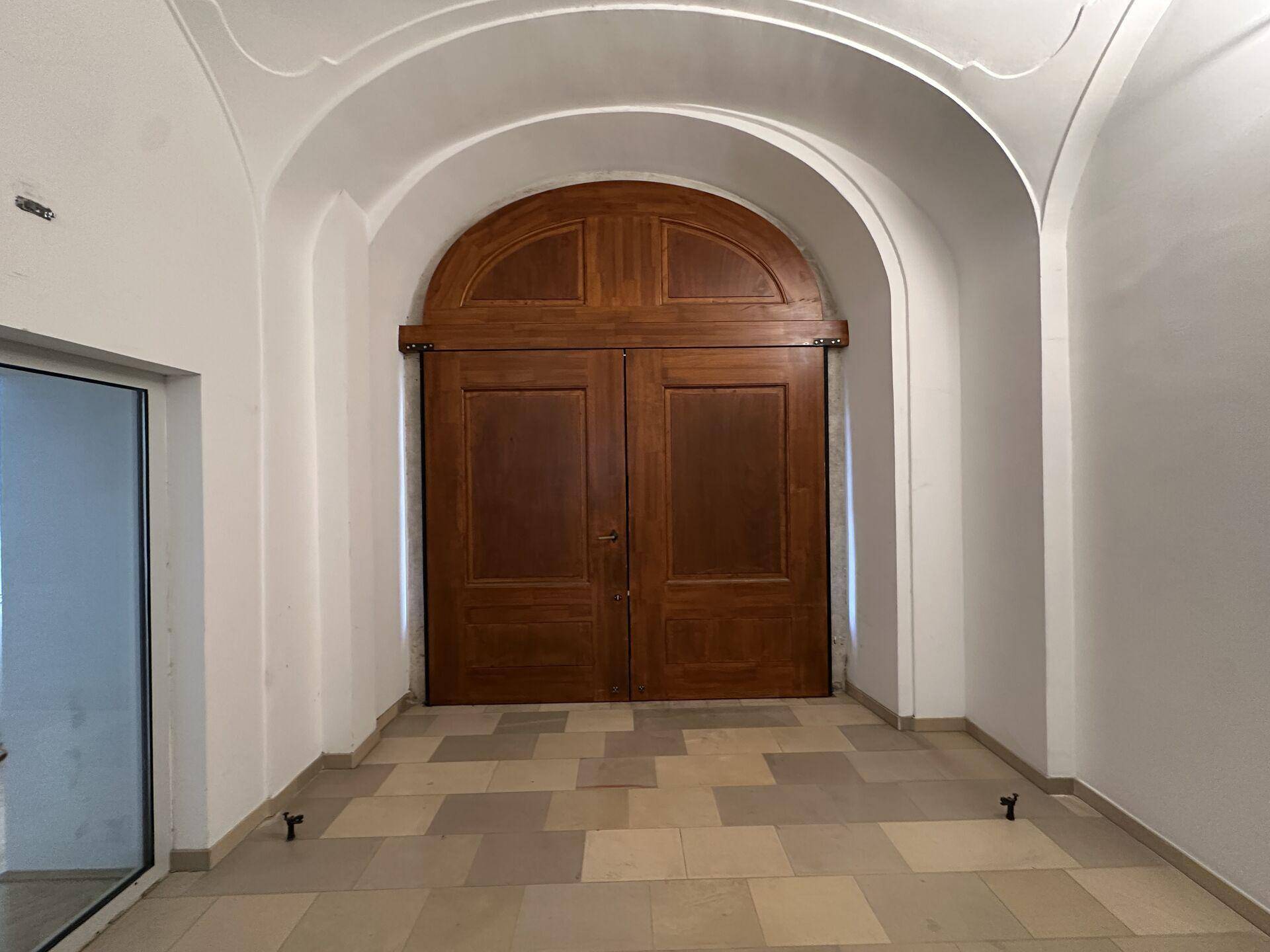 Historischer Gang mit gewölbter Decke und einer imposanten, großen Holztür am Ende.