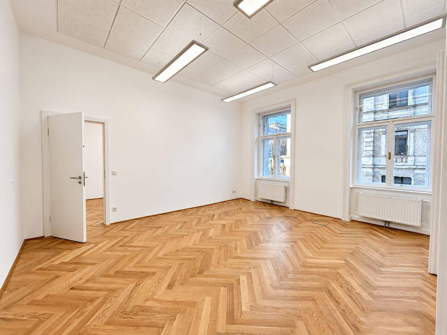Heller Büroraum mit Fischgrätparkett und abgehängter Decke, ideal für moderne Arbeitsumgebungen.
