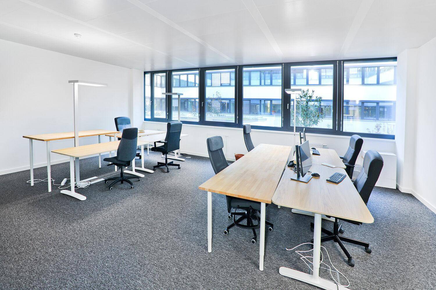 Helles und geräumiges Büro mit mehreren Schreibtischen, ergonomischen Stühlen und großen Fenstern.