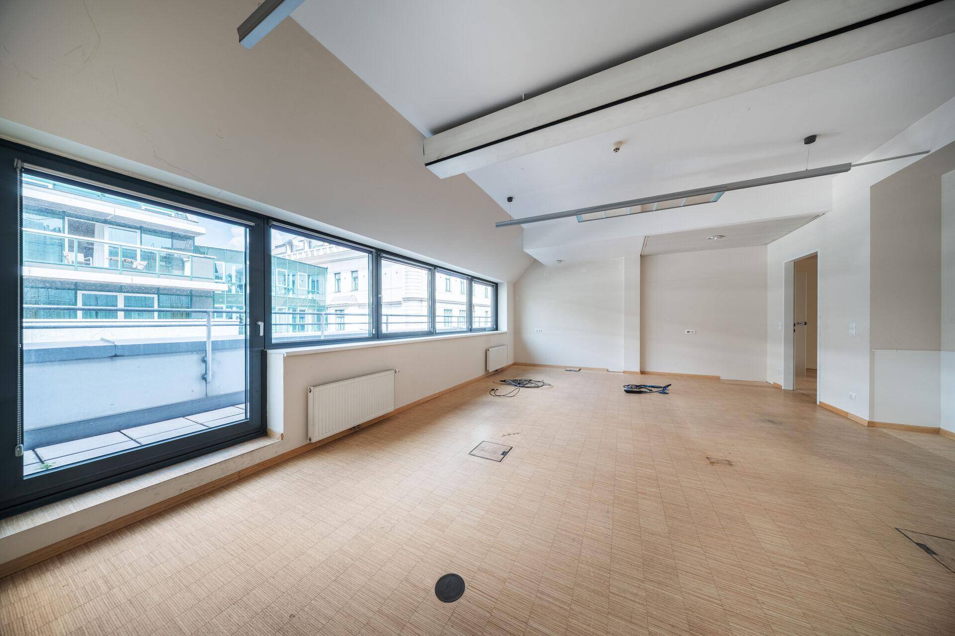 Heller Büroraum mit großen Fenstern, Zugang zu einem Balkon und Holzboden.