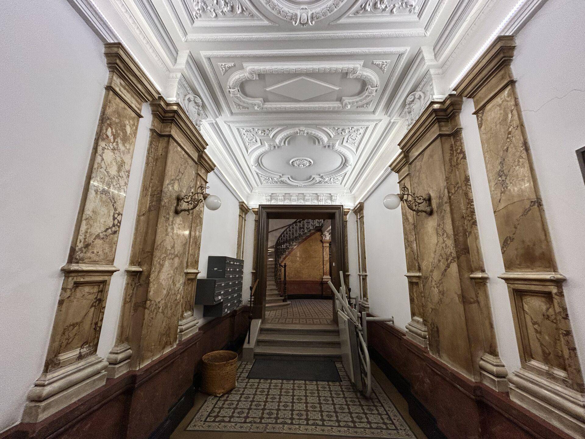 Prächtiger Eingangsbereich mit Stuckdecke, Marmorsäulen und gemustertem Fliesenboden, der zum Treppenhaus führt.
