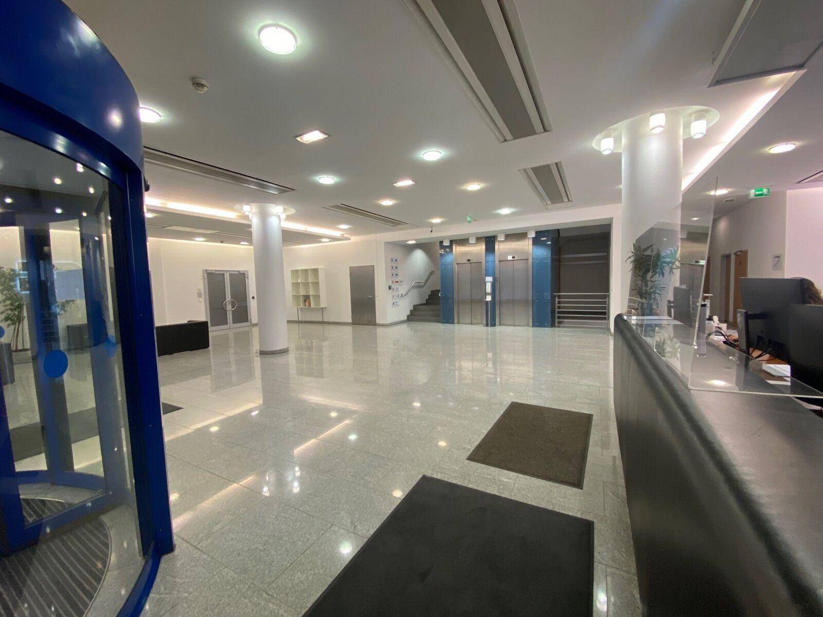Geräumige und helle Lobby mit glänzendem Fliesenboden, Rezeption, Aufzügen und modernem Design.
