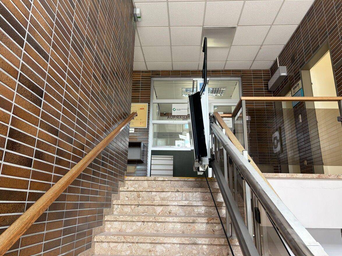 Treppenhaus mit braunen Fliesenwänden und einem Treppenlift für Barrierefreiheit.
