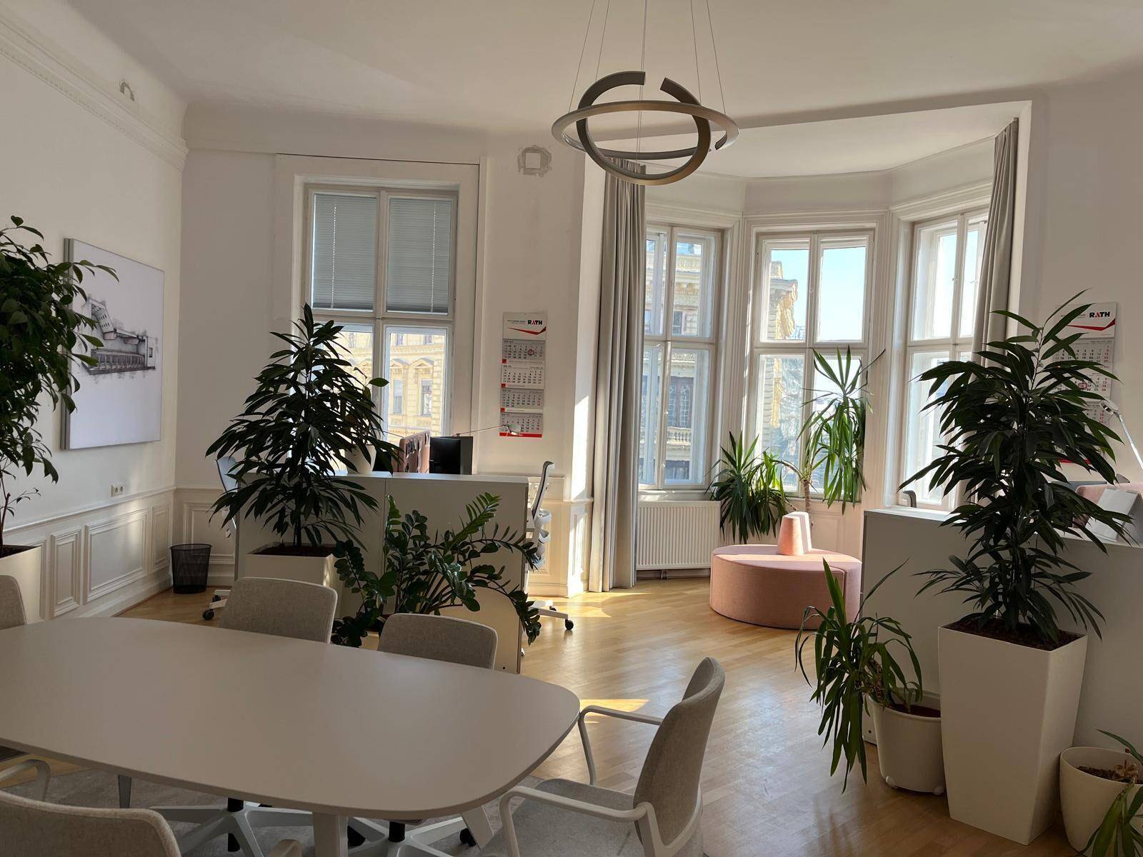 Helles Büro mit großen Fenstern, Holzboden und modernen Büromöbeln, geschmückt mit Pflanzen.