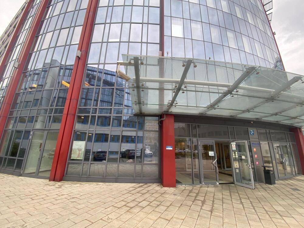 Haupteingang des modernen Bürogebäudes mit Glasvordach und roten Akzenten.
