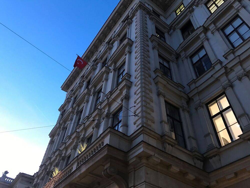 Detailaufnahme der historischen Fassade eines Gebäudes mit klassischen Verzierungen und Fenstern unter blauem Himmel.