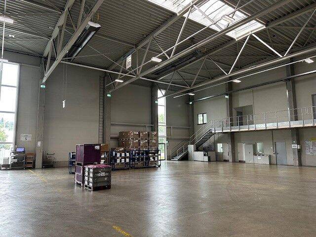 Geräumige Lagerhalle mit hohen Decken, Oberlichtern und natürlichem Lichteinfall, teilweise mit Kartons.