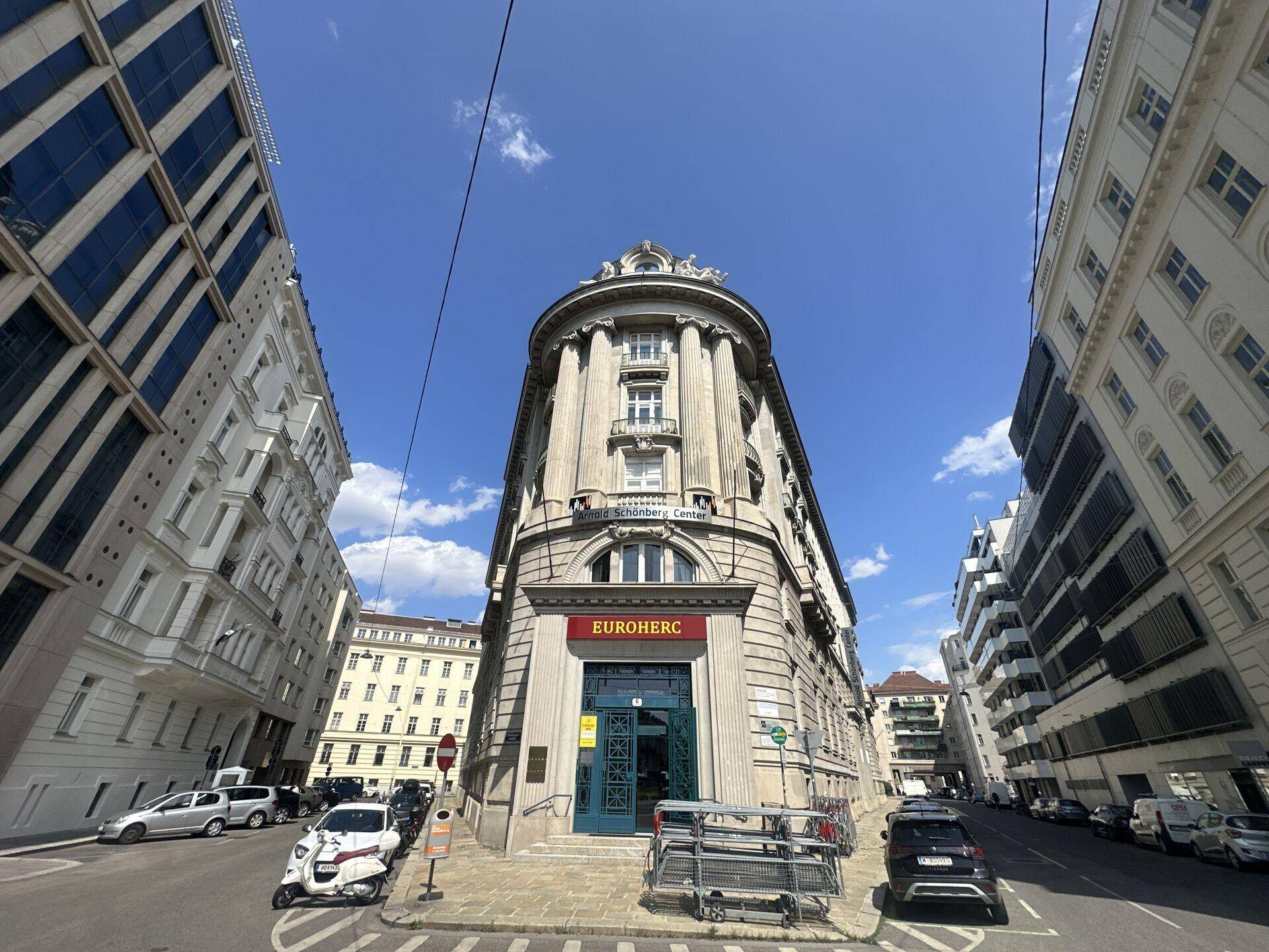 Historisches Eckgebäude mit klassischer Architektur und Geschäften im Erdgeschoss an einer belebten Straße.