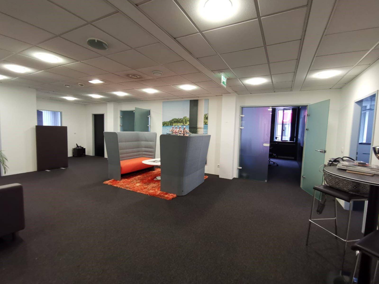 Moderner Loungebereich mit bequemen Sitzgelegenheiten, Teppichboden und Glastüren zu weiteren Büros.