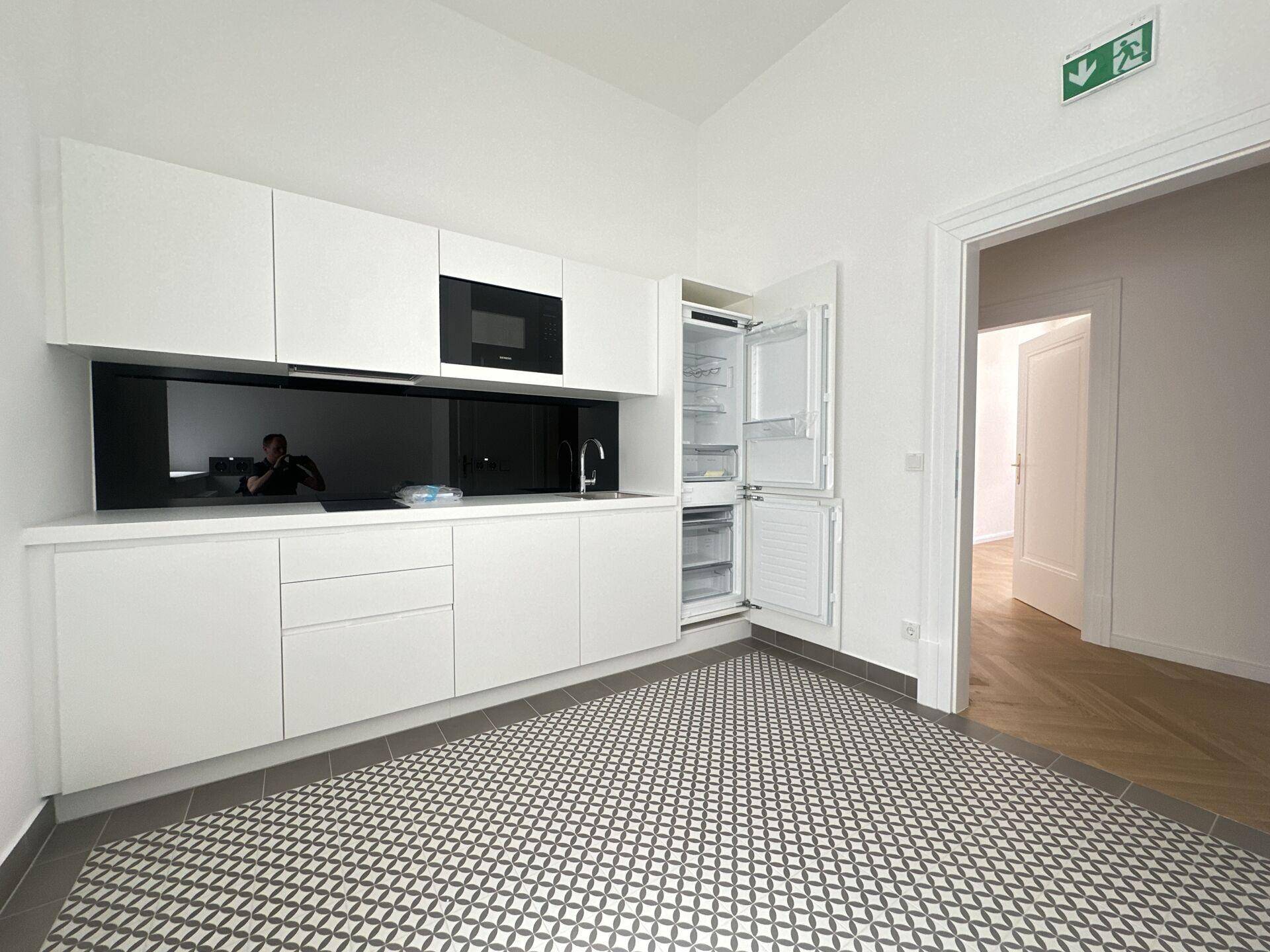 Moderne Küchenzeile mit weißen Schränken, integriertem Kühlschrank und gemustertem Fliesenboden.