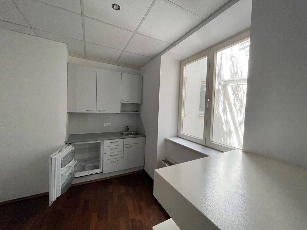 Kompakte Küchenzeile mit weißen Schränken, Spüle und Kühlschrank unter einem Fenster.