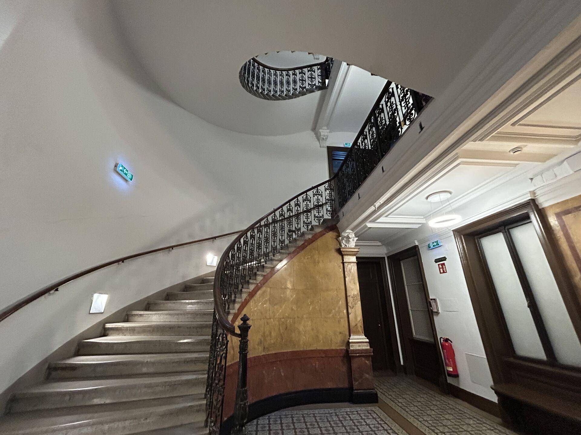Elegantes Treppenhaus mit geschwungener Marmortreppe und kunstvollen schmiedeeisernen Geländern in einem historischen Gebäude.