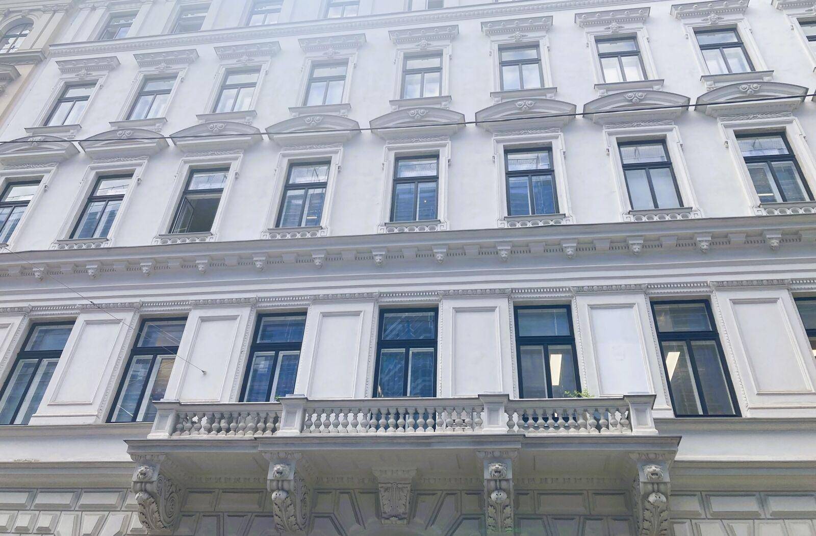 Historische Fassade eines Altbaus mit vielen Fenstern und einem verzierten Balkon im Erdgeschoss.