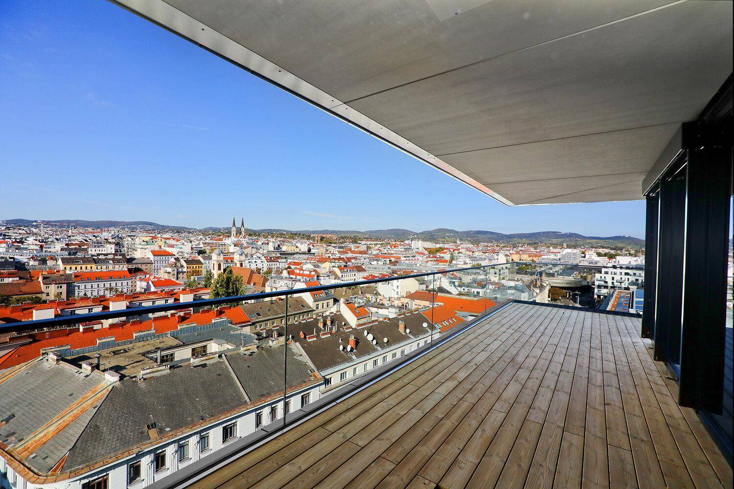 Geräumige Terrasse mit Holzboden und Glasgeländer, die einen weiten Blick über die Stadt bietet und zum Verweilen einlädt.