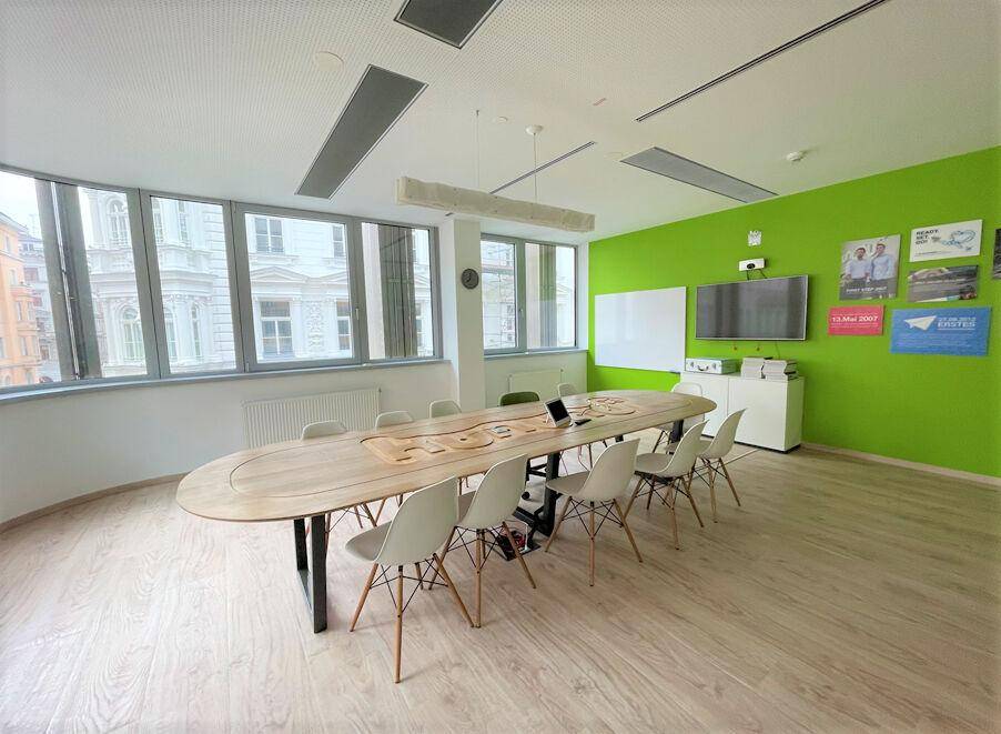 Heller Konferenzraum mit langem Holztisch, weißen Stühlen und einer auffälligen grünen Wand.