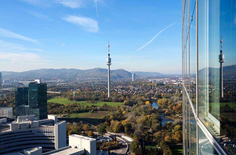 Eine weite Aussicht über eine Stadt mit Fluss, grünen Landschaften und Bergen am Horizont, aufgenommen von einem Hochhaus.