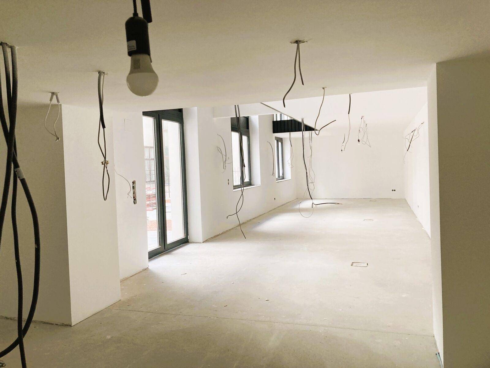Heller, unfertiger Raum mit weißen Wänden, Betonboden und großen Fenstern, bereit für die Fertigstellung.