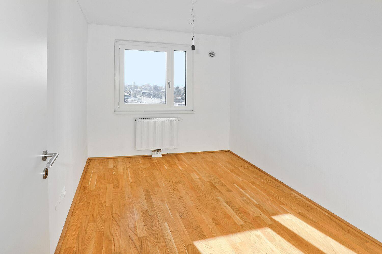 Helles Schlafzimmer mit Parkettboden und einem Fenster, das viel Tageslicht hereinlässt.