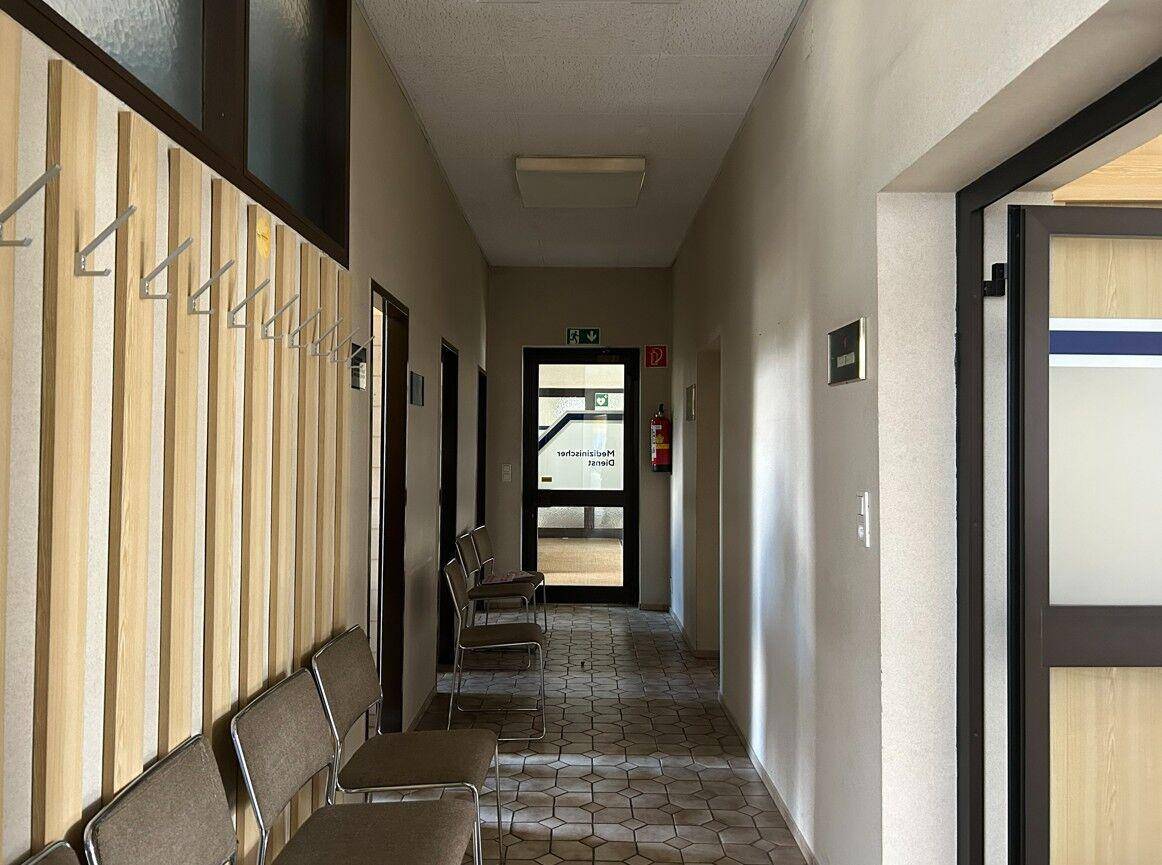 Langer Flur mit gemustertem Fliesenboden, Garderobe und Sitzgelegenheiten für Besucher.