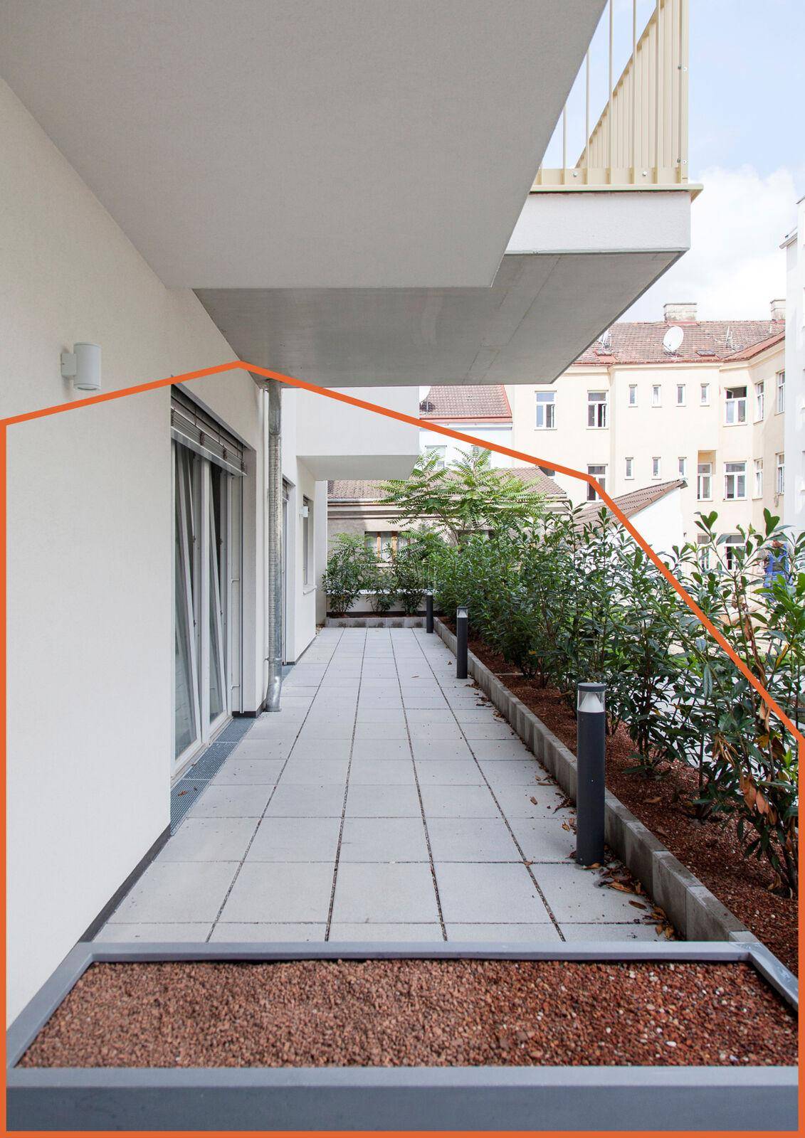 Gefliester Außenbereich oder Terrasse mit Pflanzenbeeten und Blick auf die umliegenden Gebäude.