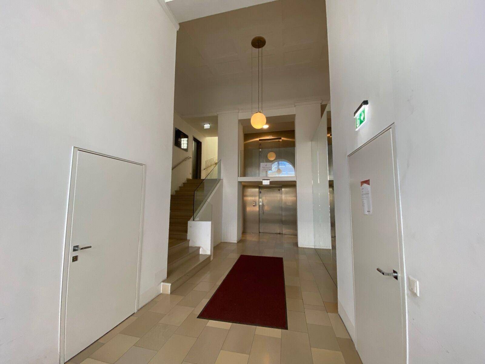 Heller Eingangsbereich mit Aufzügen, Treppenhaus und einem roten Teppich.