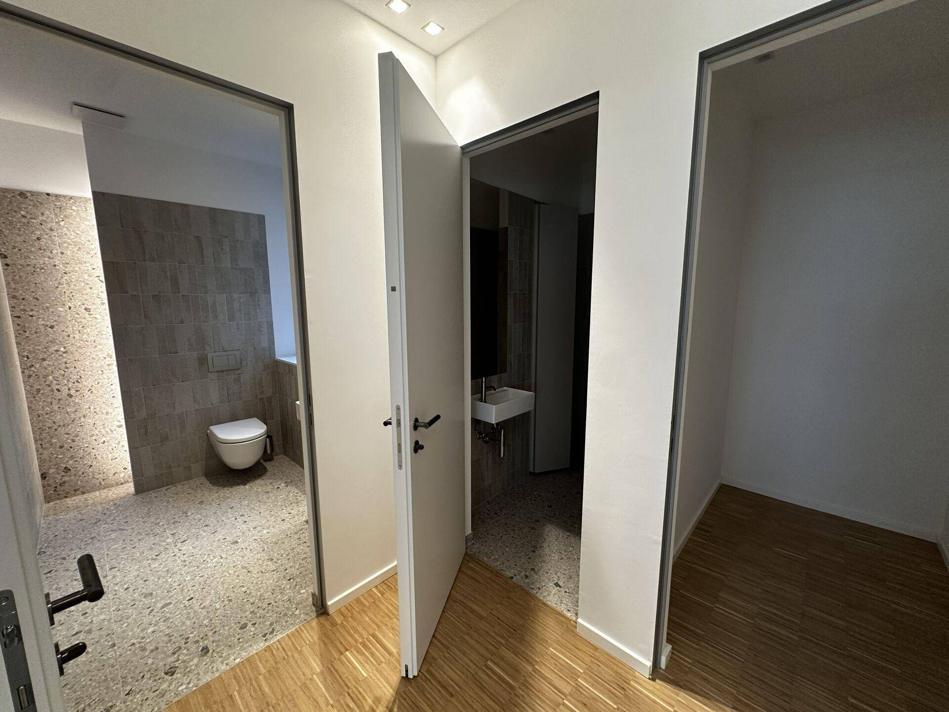 Heller Flur mit Holzboden und Zugang zu mehreren Räumen, darunter ein modernes Badezimmer.