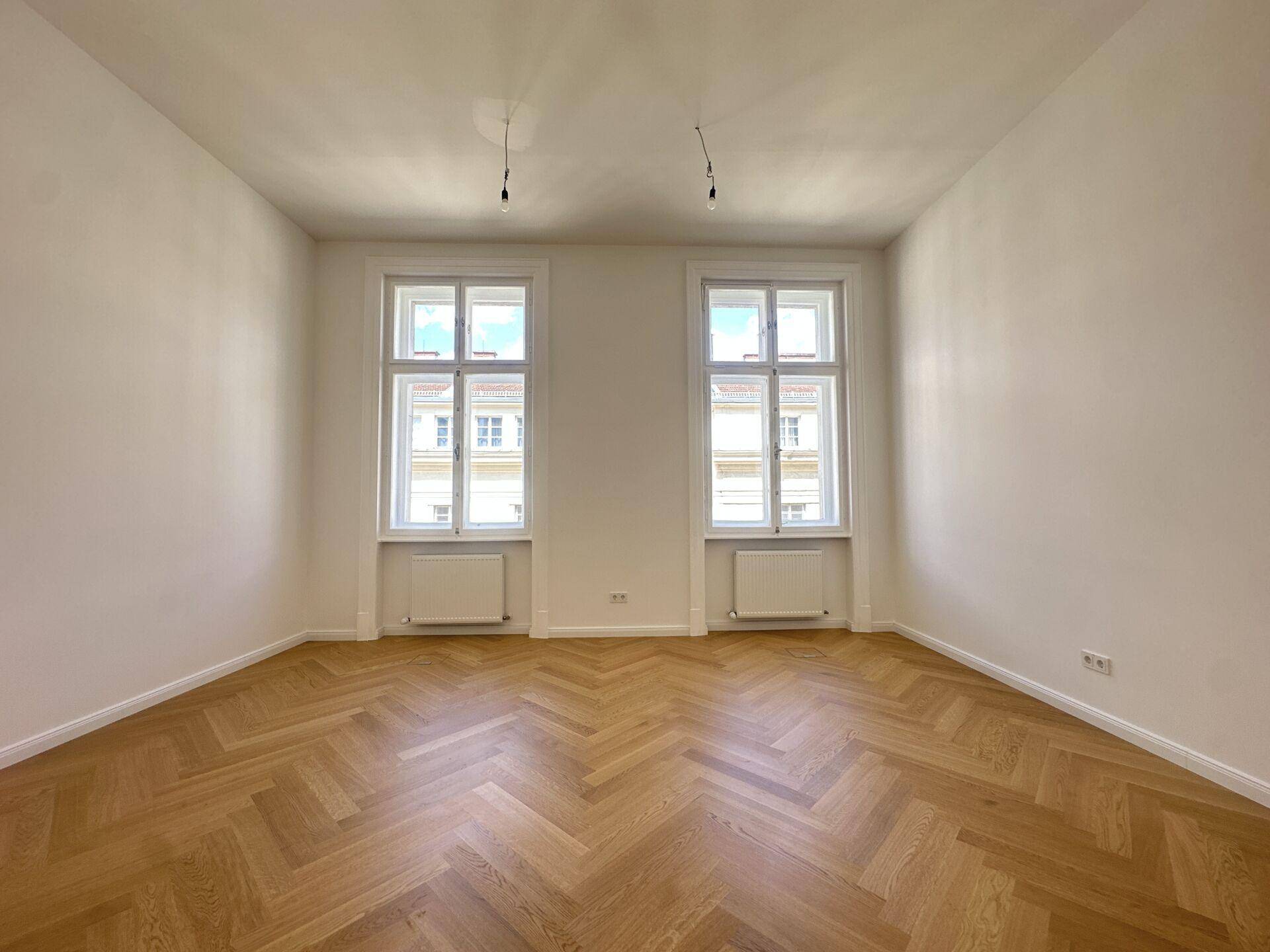 Heller Büroraum mit klassischem Fischgrätparkett und zwei großen Fenstern zur Straße.