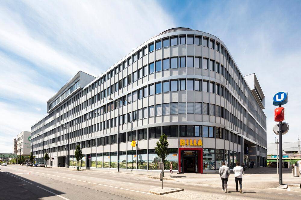 Großes, modernes Bürogebäude mit abgerundeter Ecke, Geschäften im Erdgeschoss und U-Bahn-Zugang.