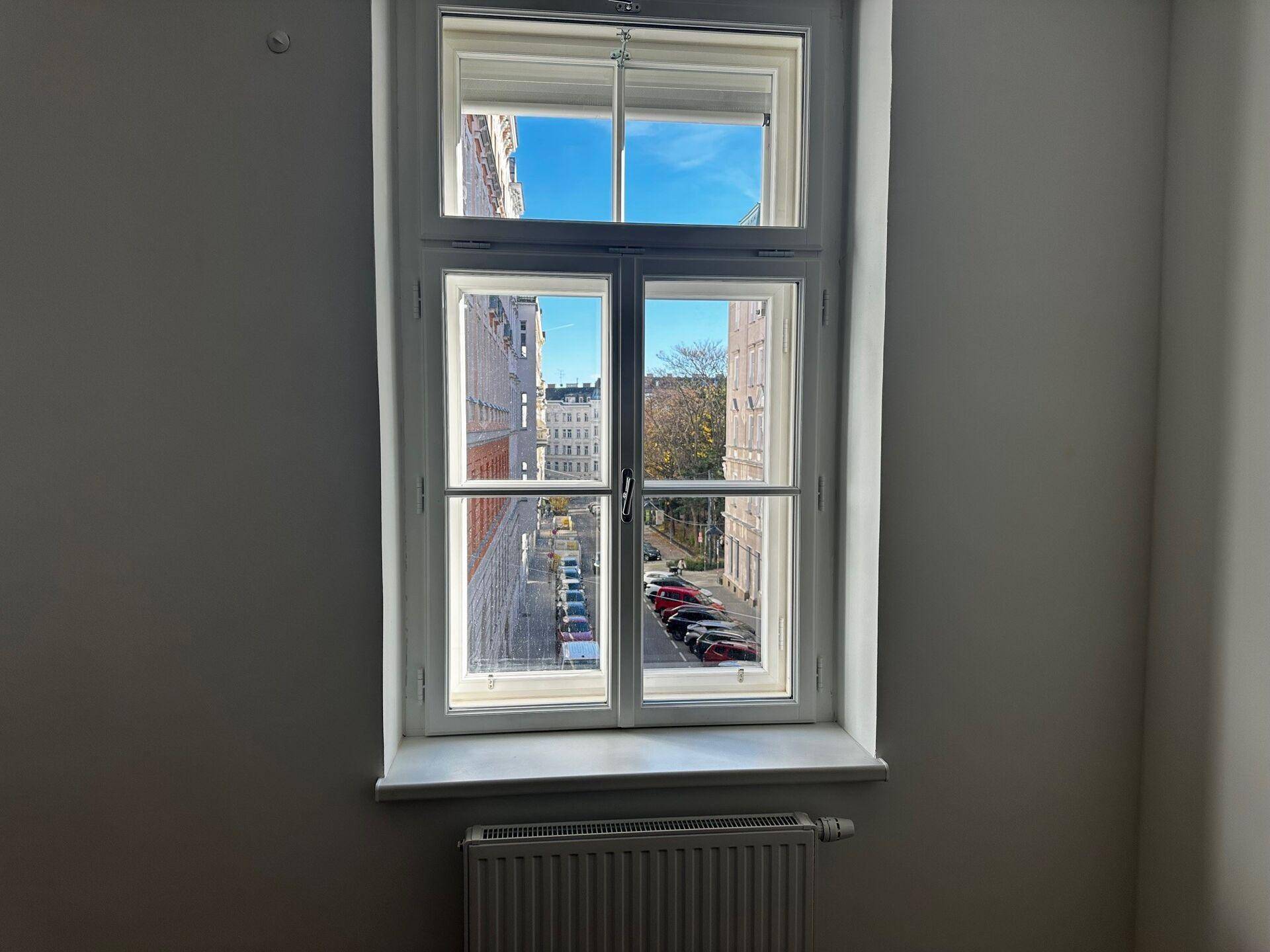 Fenster in einem Büro mit Blick auf die Straße und gegenüberliegende Gebäude unter blauem Himmel.