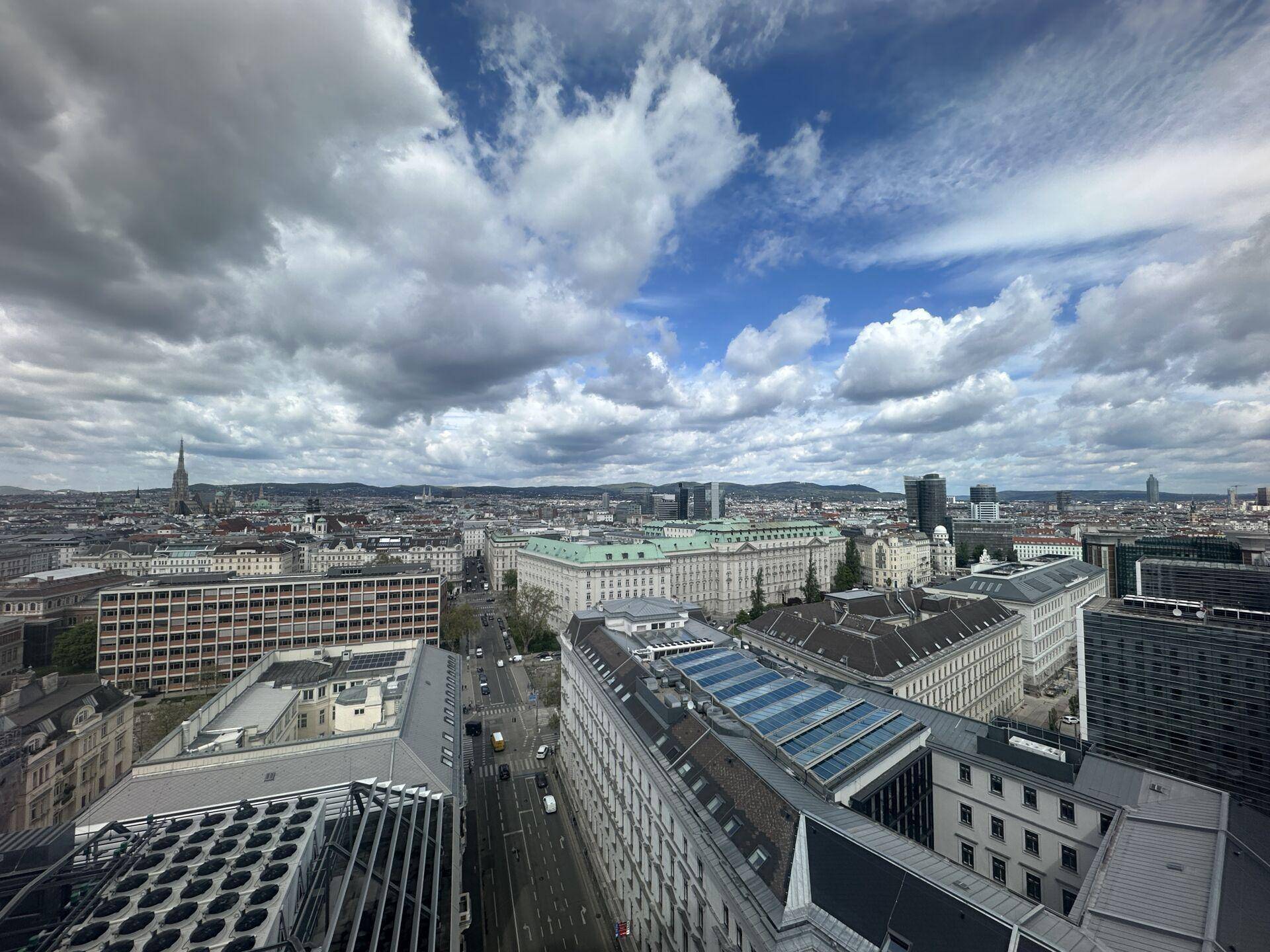Panoramablick über die Stadt mit historischen und modernen Gebäuden unter einem weiten Himmel mit Wolkenformationen.
