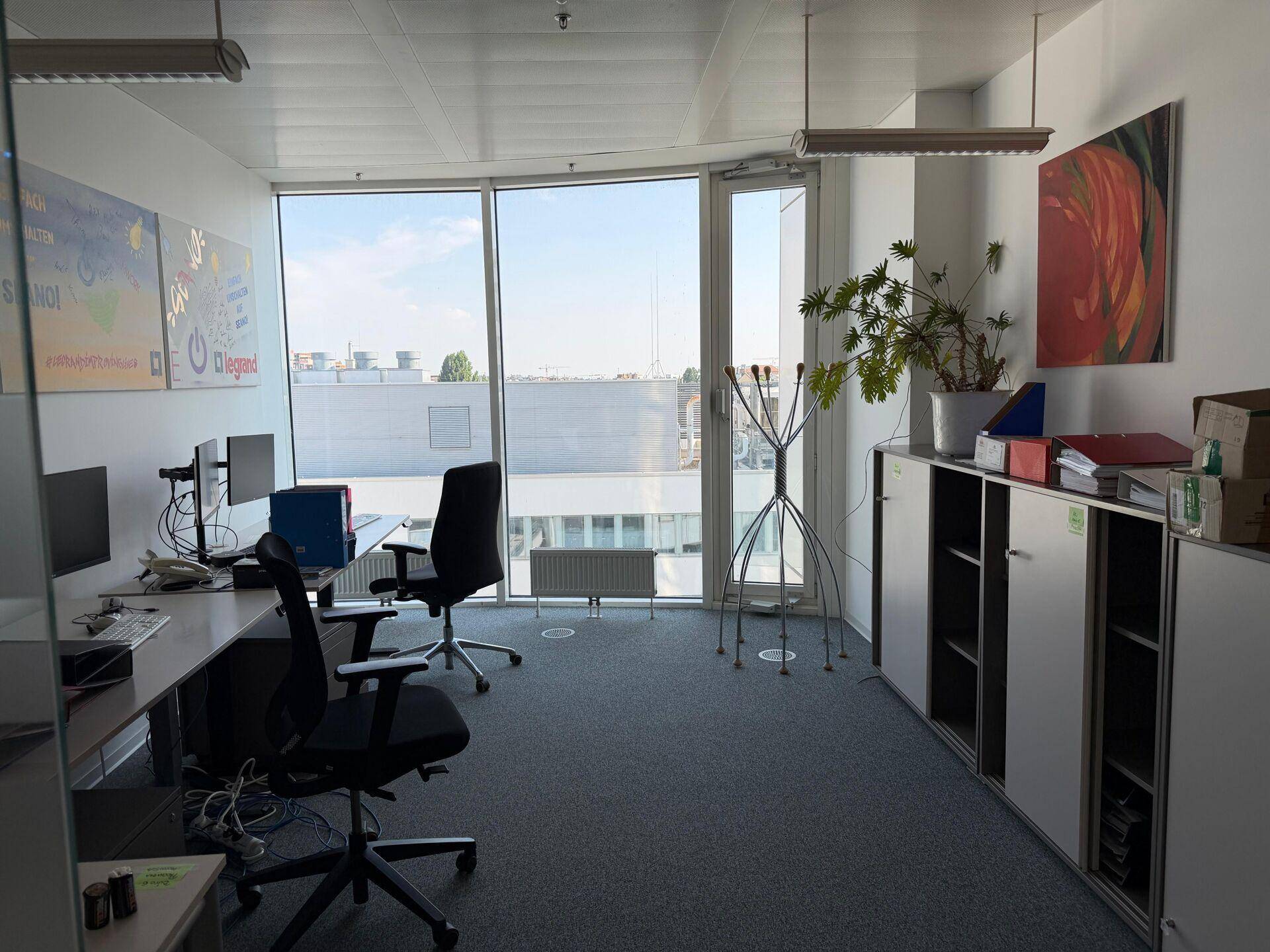 Helles Büro mit großen Fenstern, zwei Arbeitsplätzen und Blick auf die Stadt.