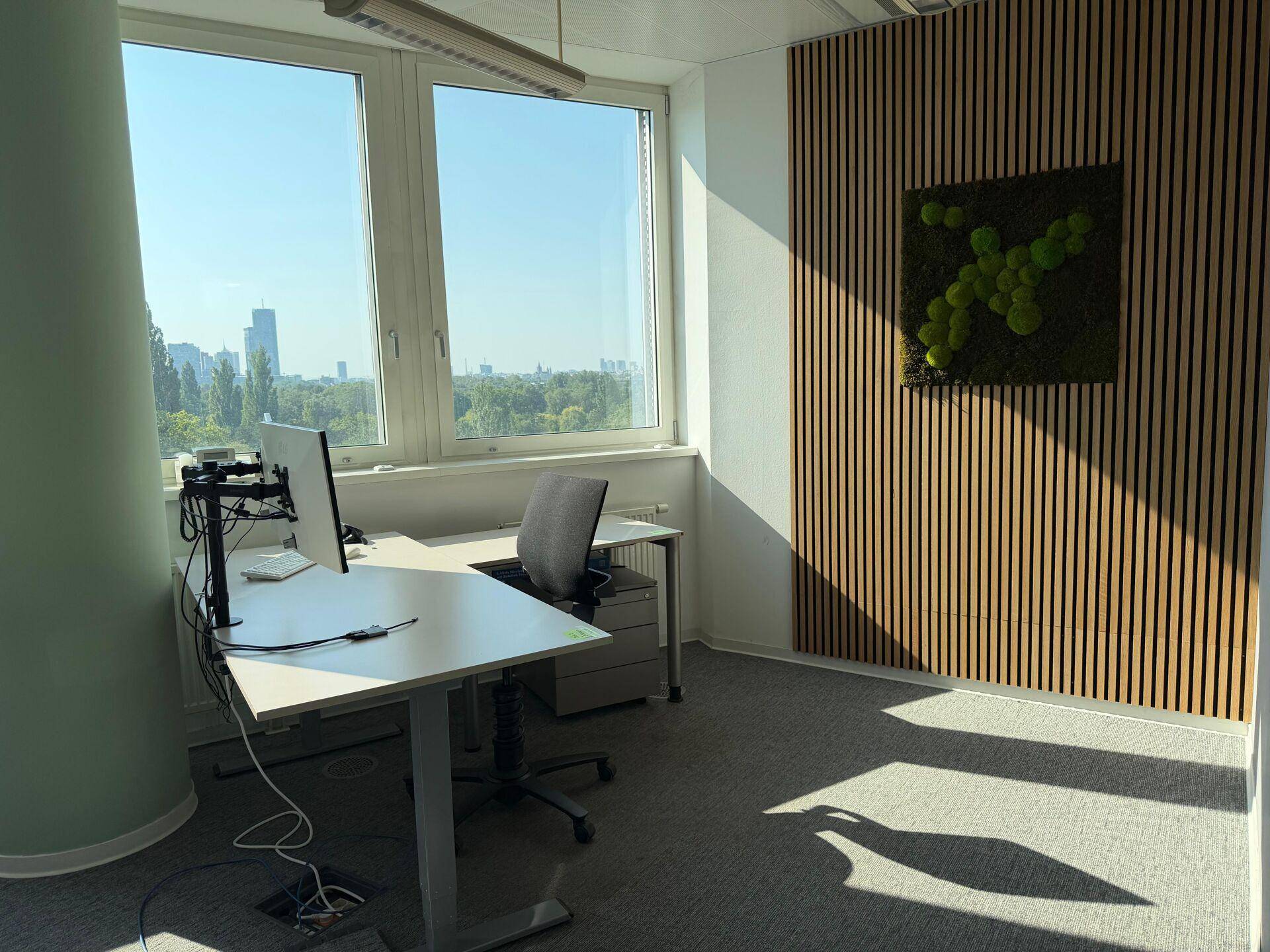 Einzelbüro mit modernem Schreibtisch, großen Fenstern und einer dekorativen Holzwand mit Moosbild.