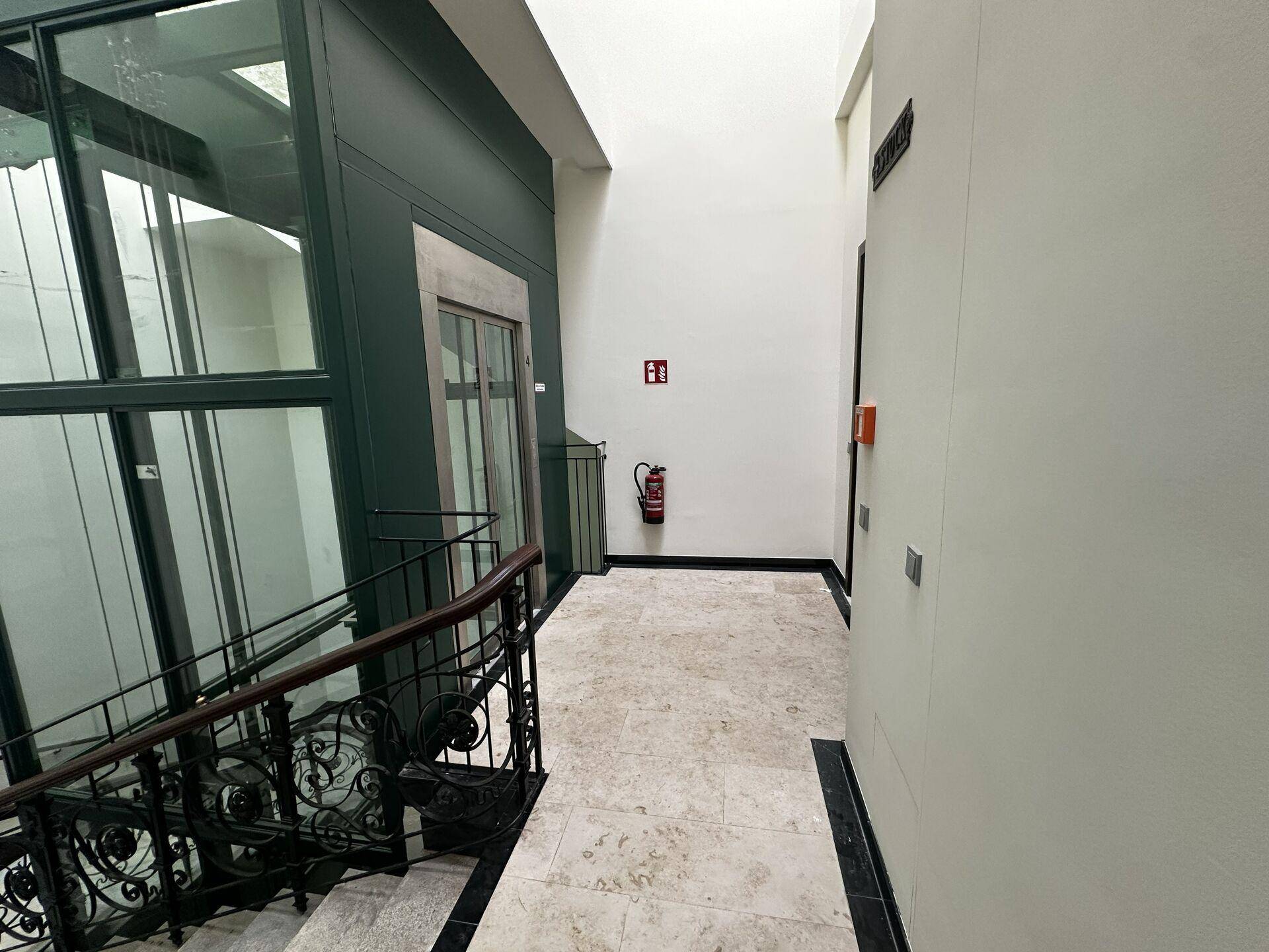 Eingangsbereich mit eleganter Treppe, modernem Aufzug und hellem Steinboden.