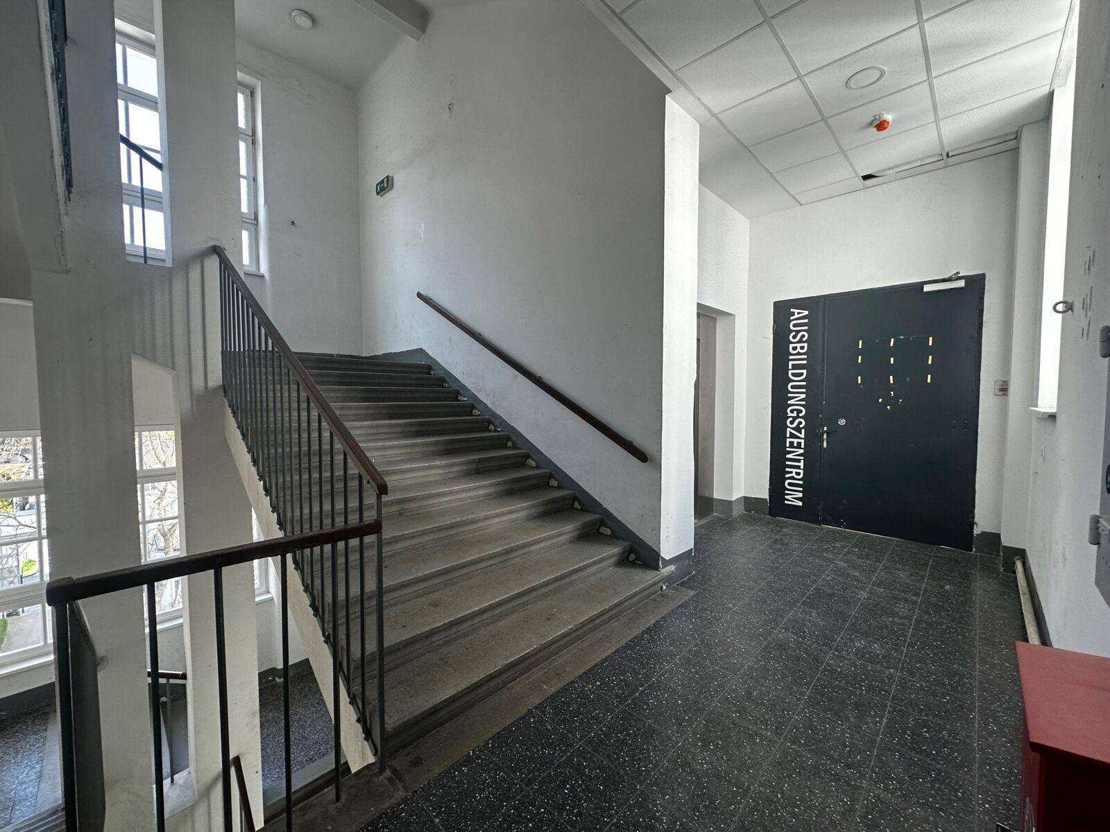 Geräumiges Treppenhaus mit dunklem Terrazzoboden und einem Schild zum Ausbildungszentrum.