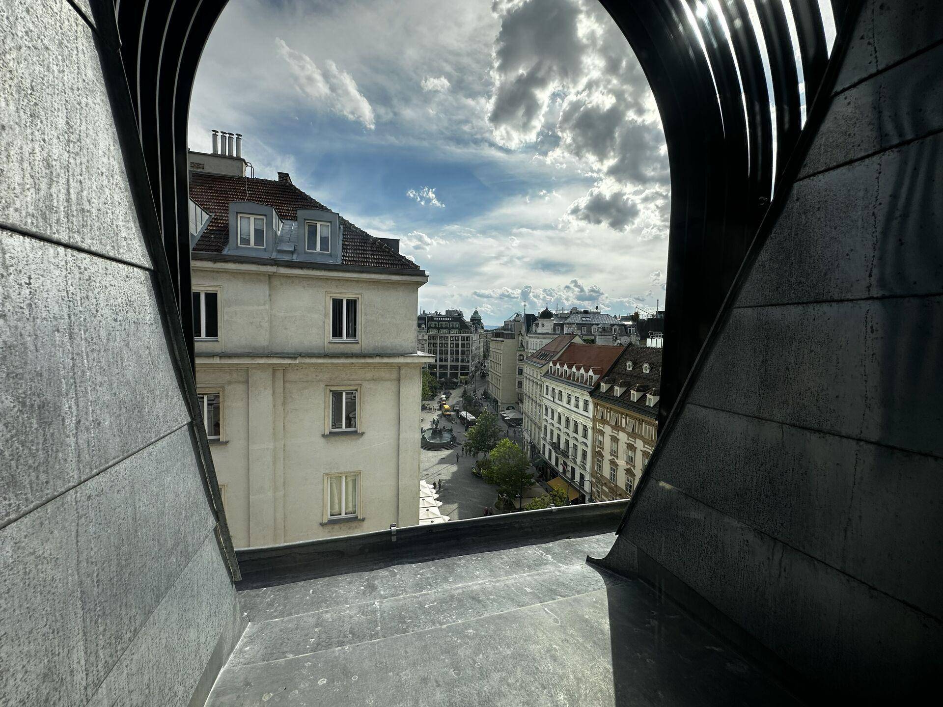 Blick aus einem Rundbogenfenster auf eine belebte Stadtstraße mit historischen Gebäuden.