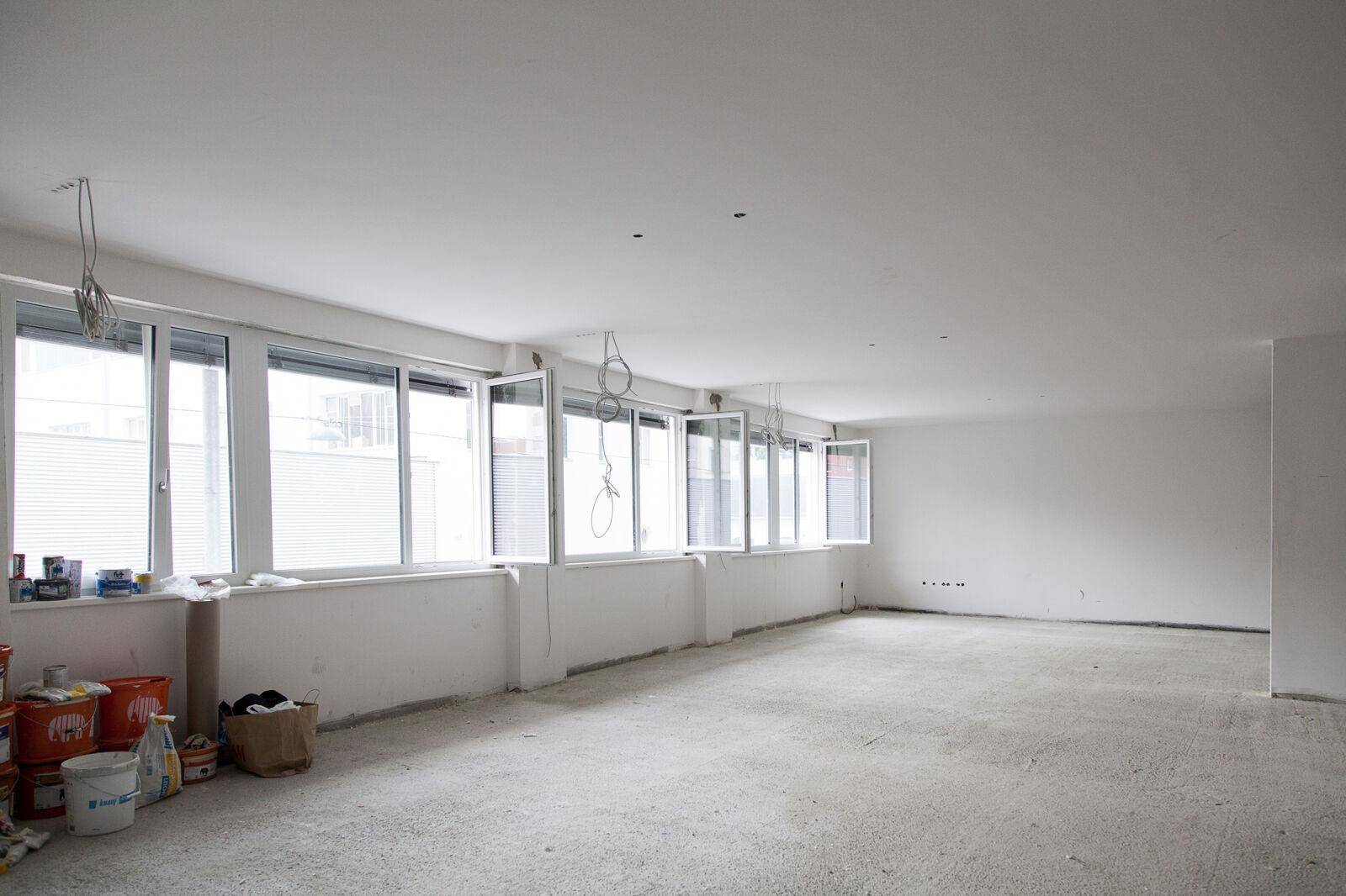 Großer, unfertiger Raum mit Betonboden, vielen Fenstern und vorbereiteten Installationen für den weiteren Ausbau.