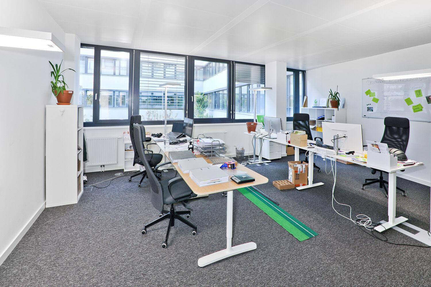 Geräumiges Büro mit mehreren Arbeitsplätzen, großen Fenstern und Teppichboden.