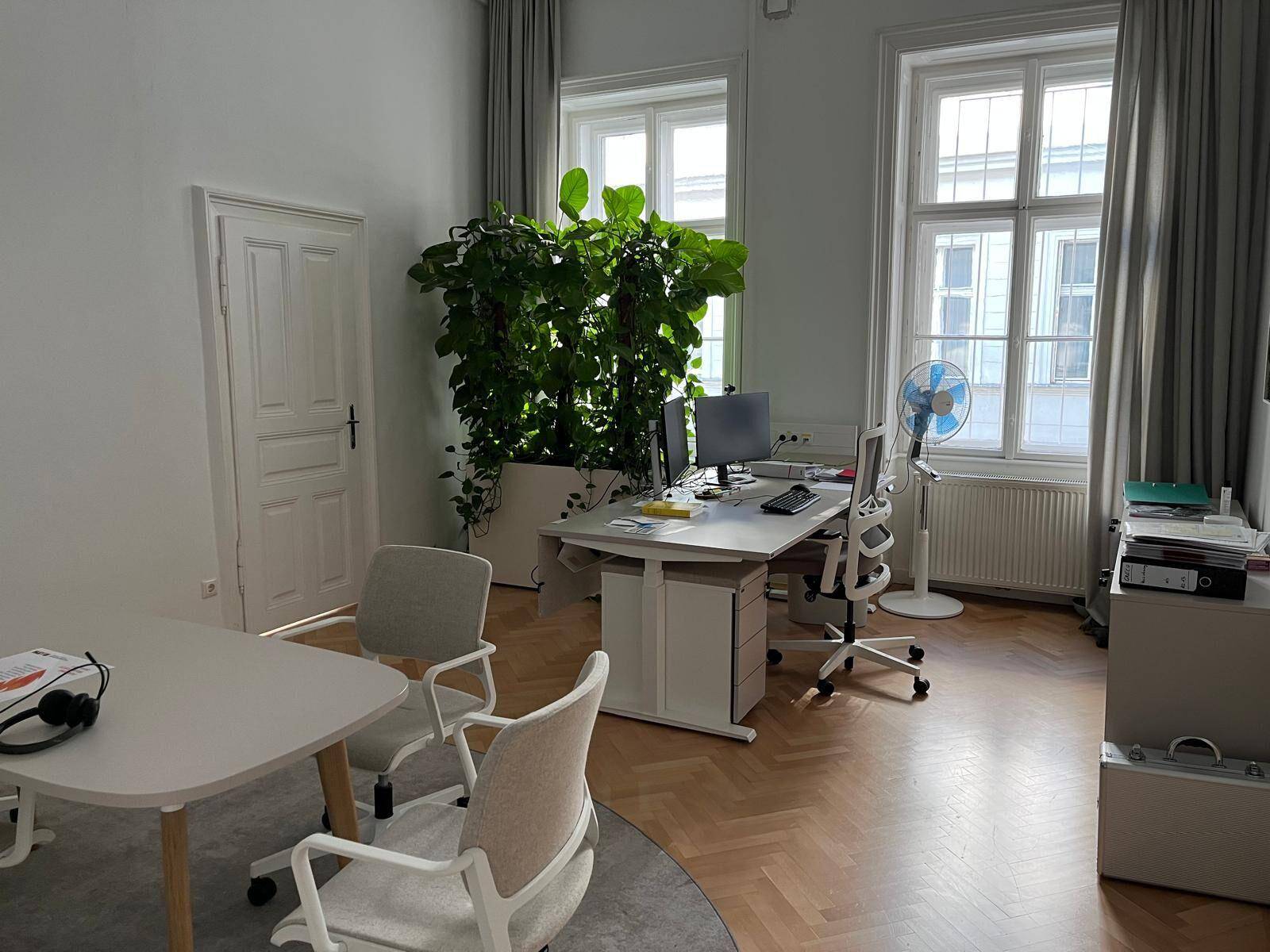 Geräumiges Büro mit Schreibtisch, ergonomischem Stuhl und großen Fenstern, beleuchtet von Tageslicht.