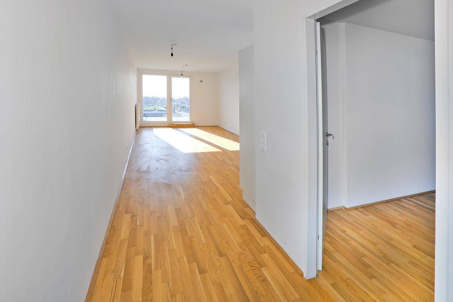 Heller Wohnbereich mit Parkettboden und Zugang zu einem Balkon oder einer Terrasse.