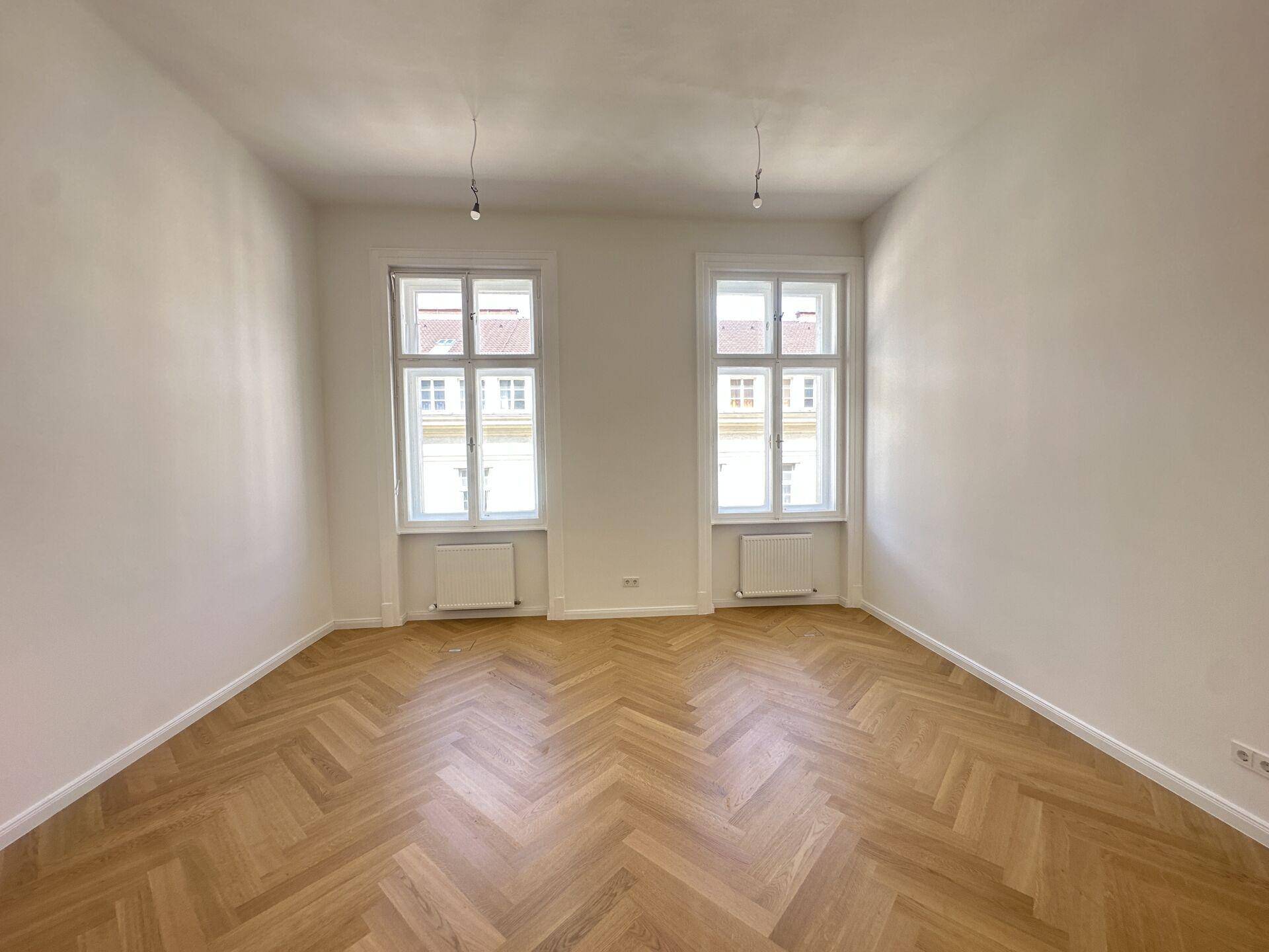 Heller Büroraum mit klassischem Fischgrätparkett und zwei großen Fenstern zur Straße.