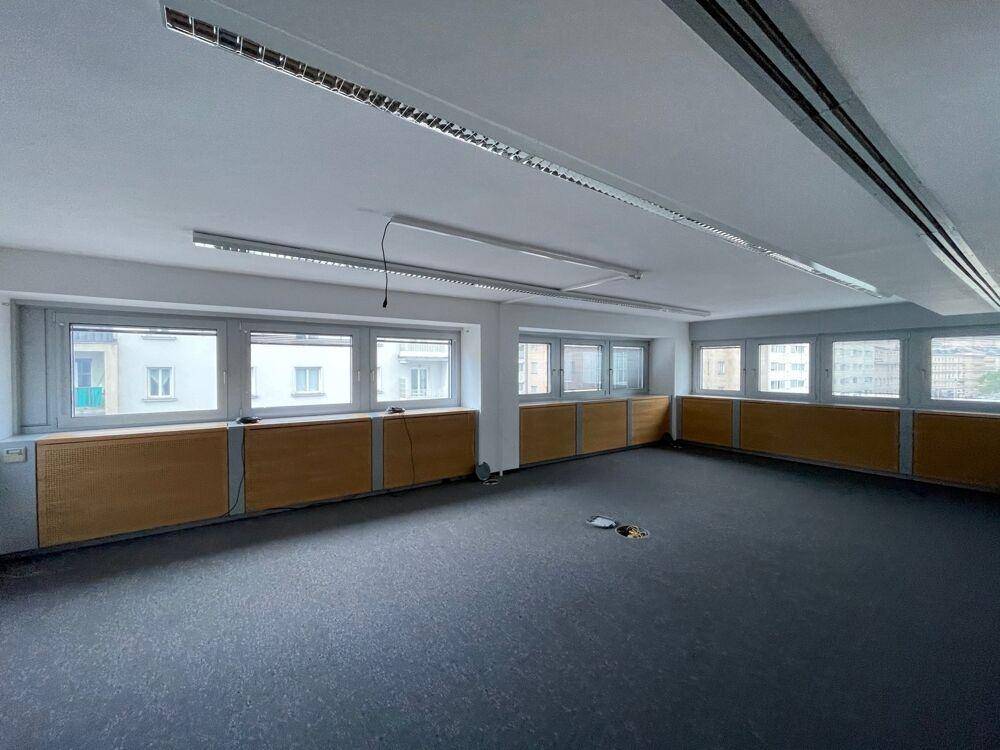 Leeres Büro mit Teppichboden, vielen Fenstern und Holzverkleidung unter den Fensterbänken.