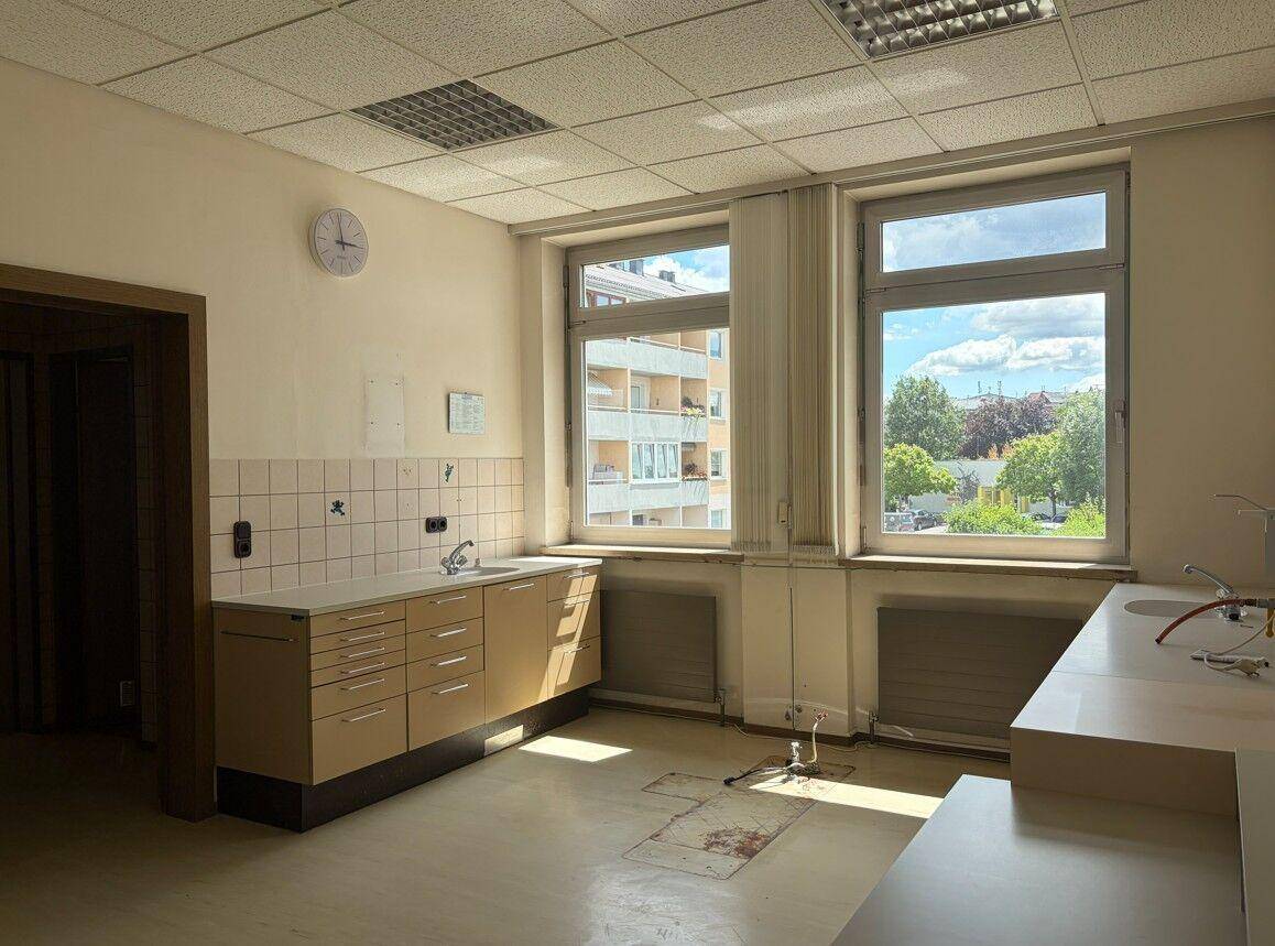 Heller Raum mit großen Fenstern, Spülbecken und Schränken, möglicherweise ein Behandlungszimmer.