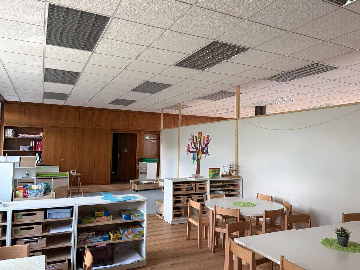 Freundlicher Spielraum mit Holzboden, niedrigen Regalen und bunten Dekorationen für Kinder.